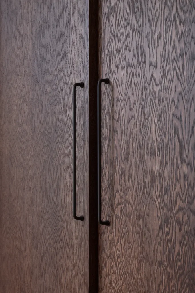 A close-up of two dark stained oak cabinet doors with dramatic grain patterning, fitted with slim matte black handles.